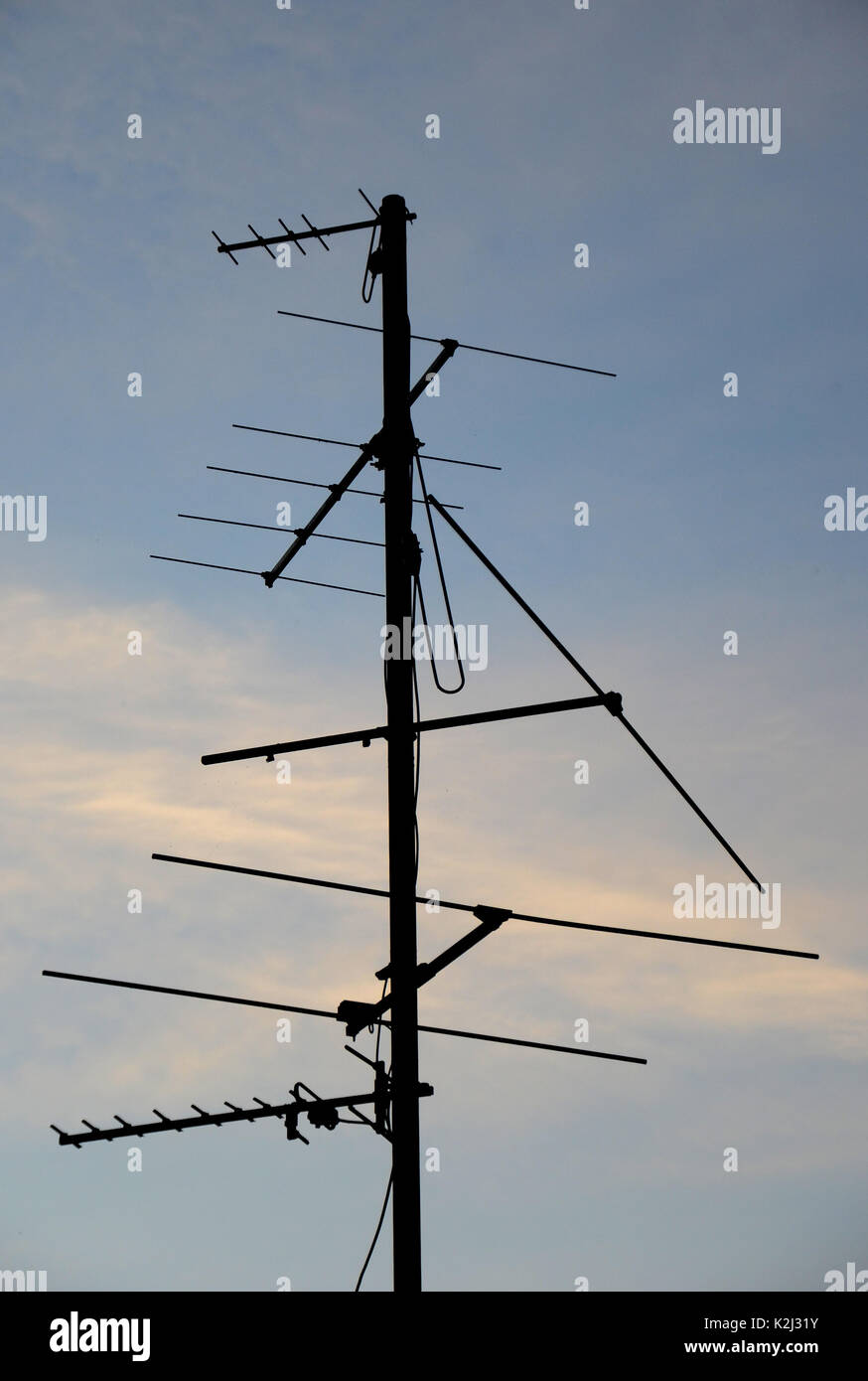 Aerial antenna for analog TV signal reception seen as silhouette against a blue eveing sky with light cirrus clouds. . Stock Photo
