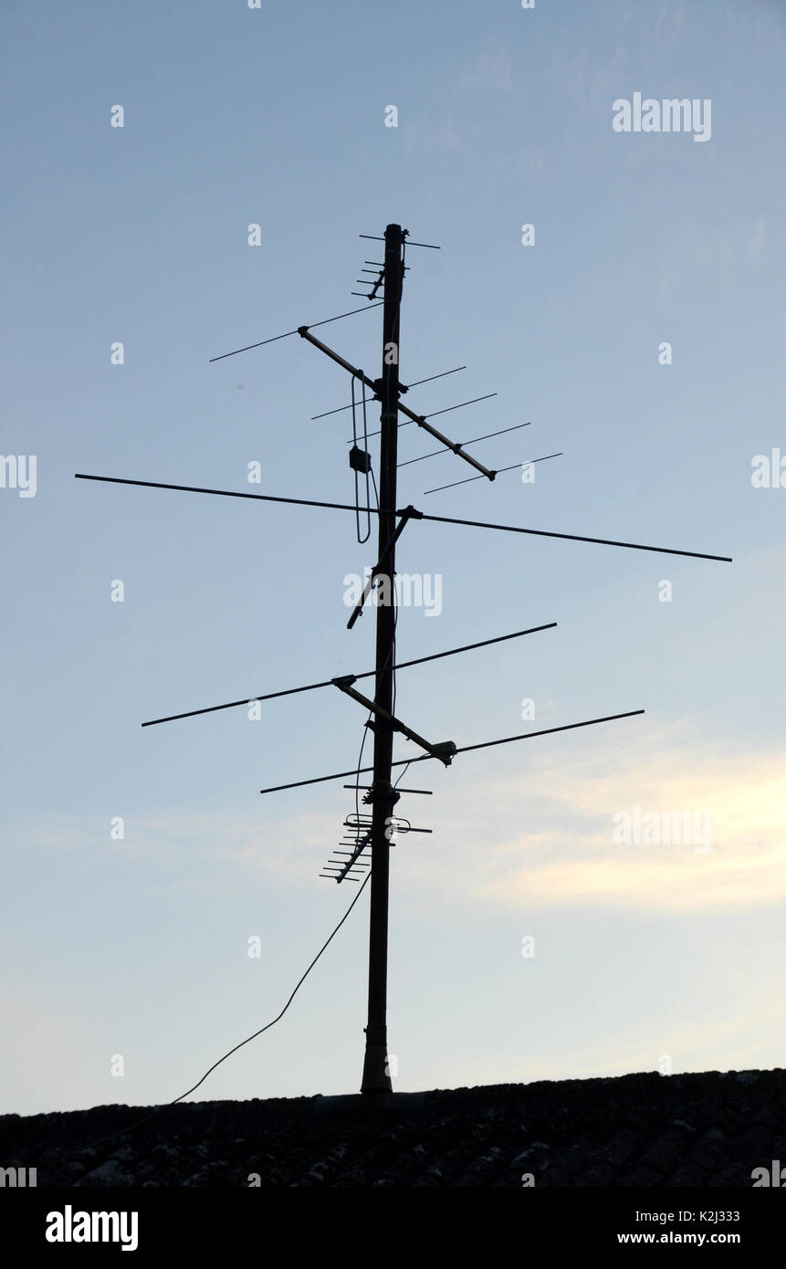 Aerial antenna for analog TV signal reception seen as silhouette against a blue eveing sky with light cirrus clouds. . Stock Photo