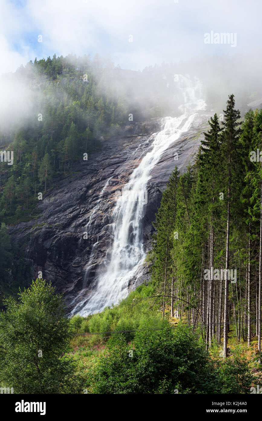 Water cascading and foaming in woodland waterfall. Clouds glide by in the high section of the fall and surrounding forest. Location Reiarsfossen in so Stock Photo