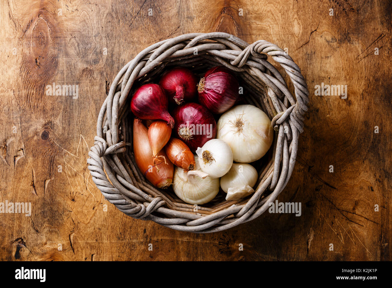 Different types of onions in basket on wooden background Stock Photo