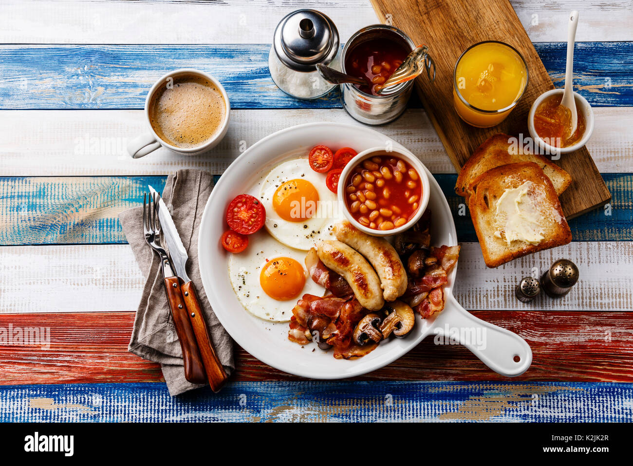 Cook Breakfeast Full English breakfast in white pan with fried eggs, sausages, bacon ...