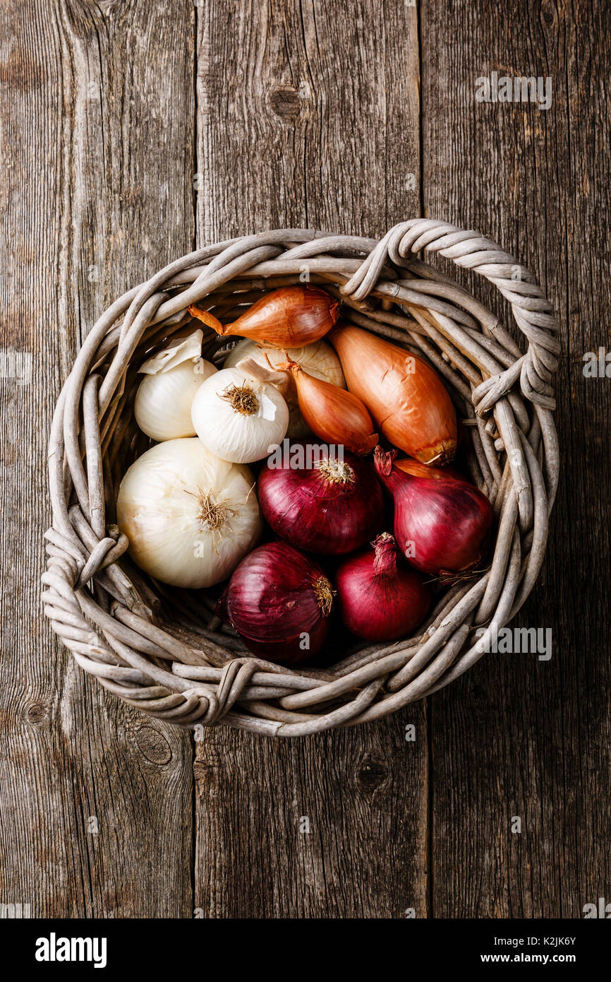 Different types of onions in basket on wooden background Stock Photo