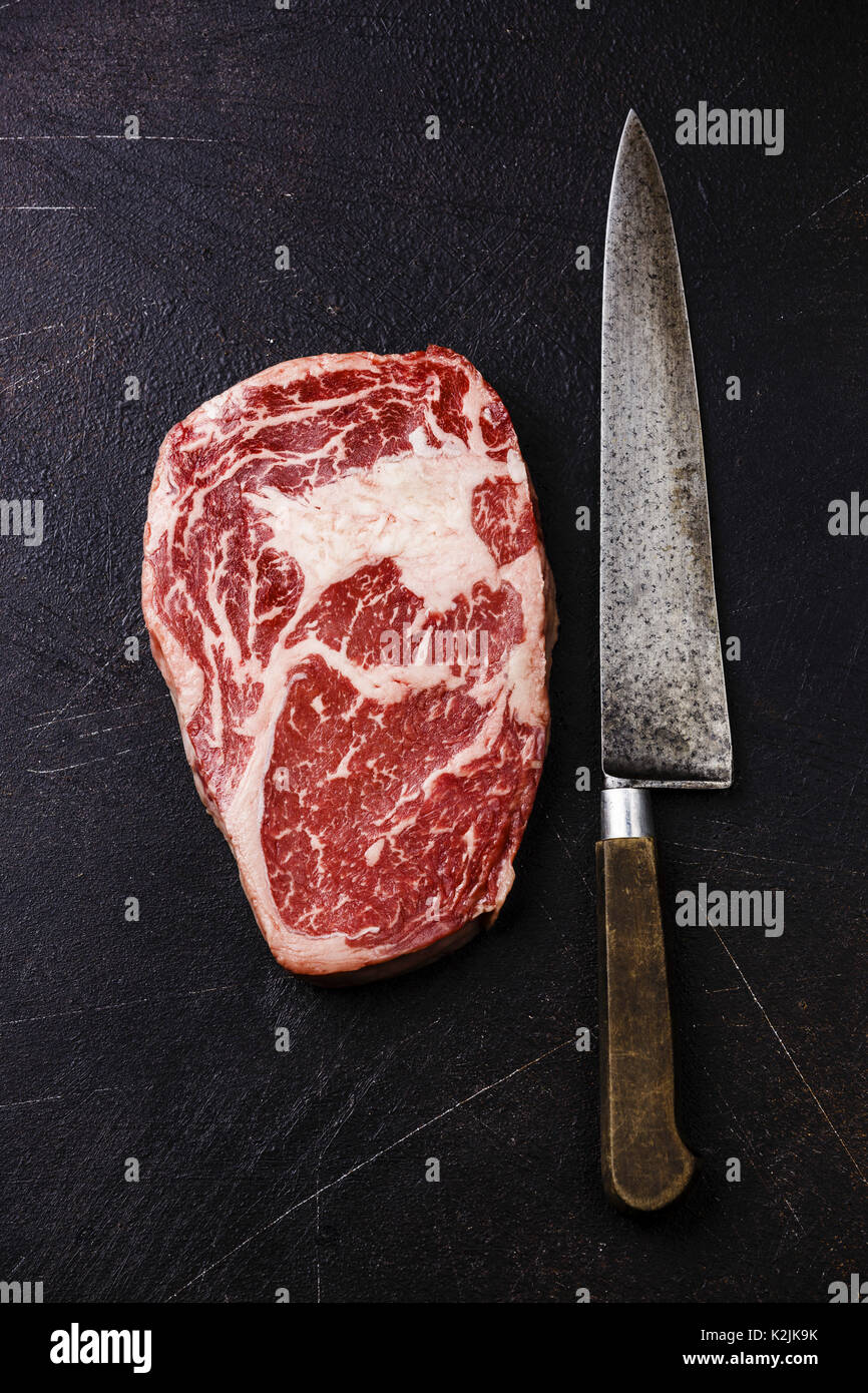 Raw fresh marbled meat Steak Rib eye Black Angus and kitchen knife on dark background Stock Photo