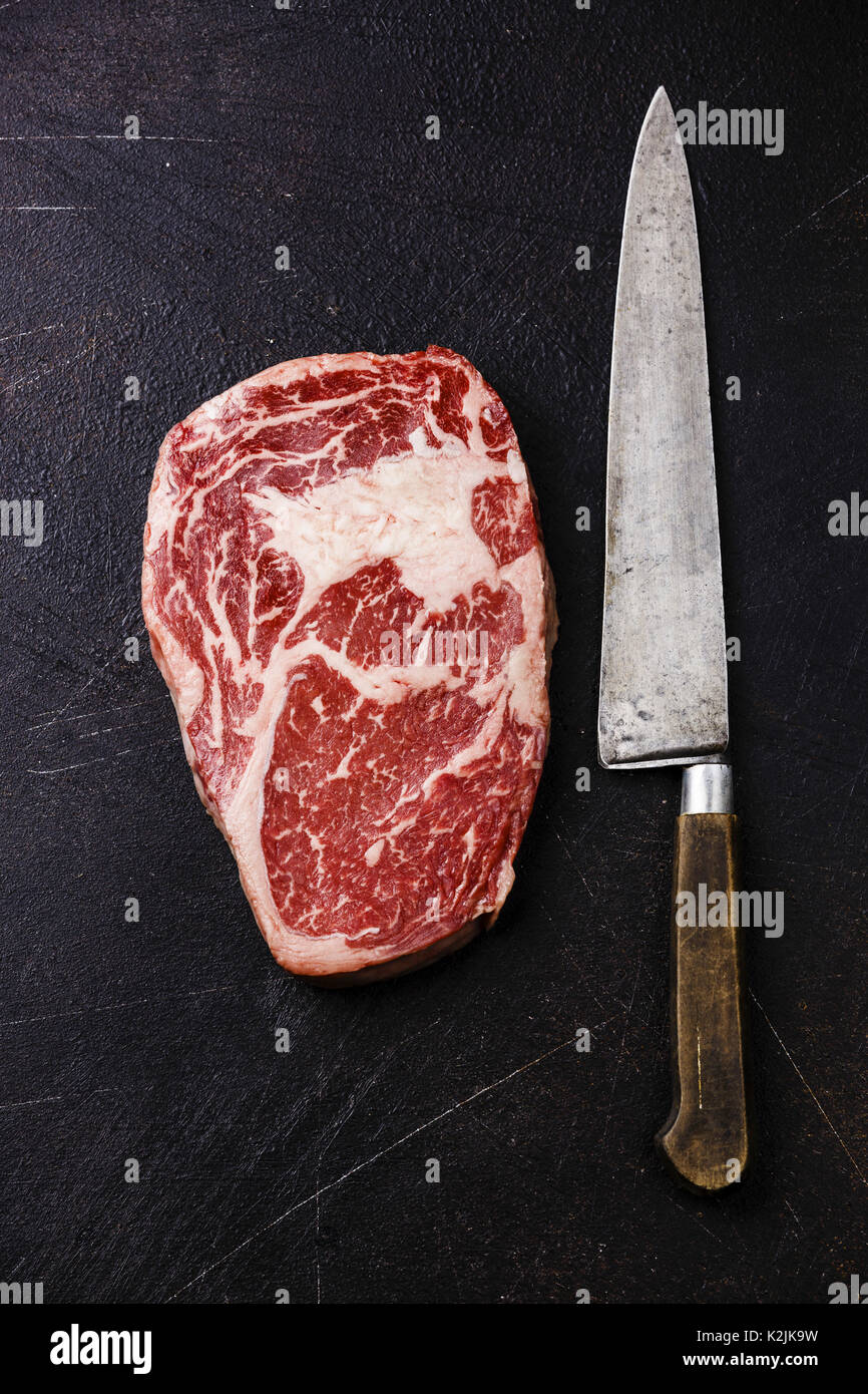 Raw fresh marbled meat Steak Rib eye Black Angus and kitchen knife on dark background Stock Photo