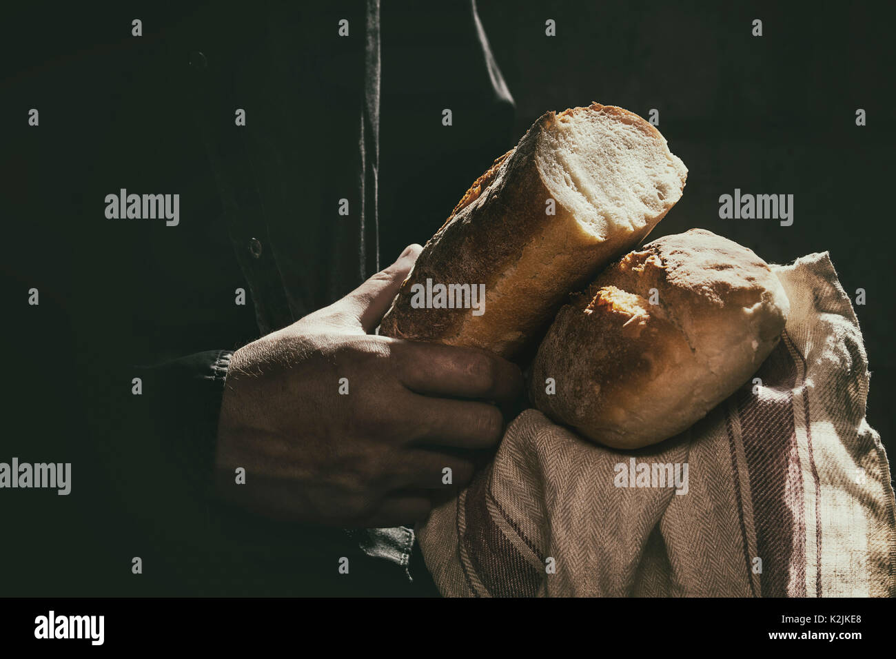 Loaf of fresh baked wheat bread in man's hands in sunshine. Rustic day light in dark room. Toned image Stock Photo