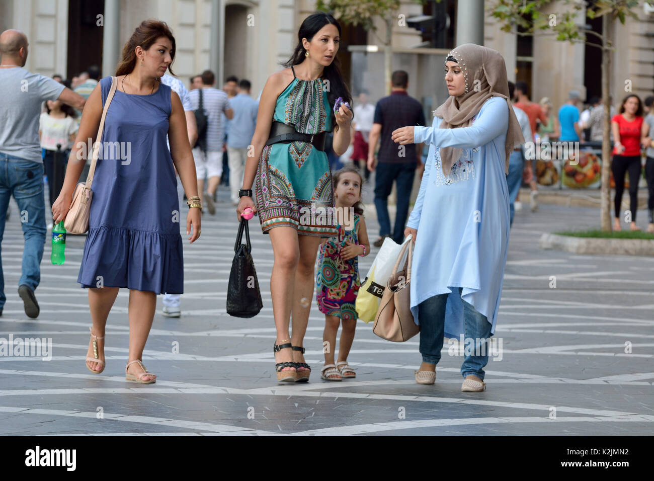 Woman wearing hijab and a woman in miniskirt with kid on the Fountains Square in Baku. Stock Photo