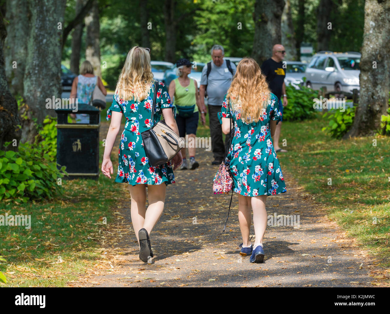 Pair of young women dressed in identical Summer dresses walking in Summer. 2 of a kind concept. Twins. Note: The women may or may not be related. Stock Photo