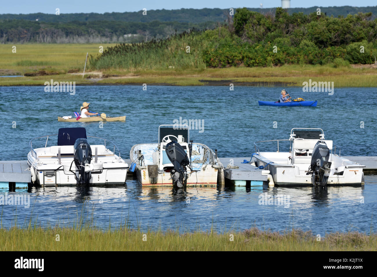 Kayakers pass by a town dock with boats at the ready - Bass Hole - Yarmouthport Stock Photo