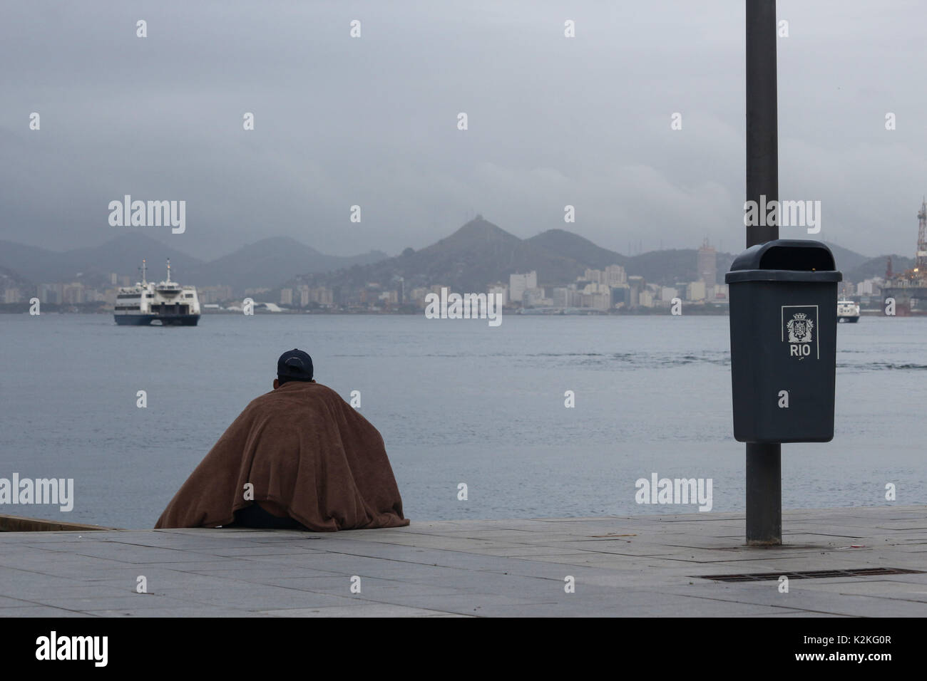Rio de Janeiro, Brazil, August 31, 2017: End of August is marked by falling temperatures in the city of Rio de Janeiro. The thermometers marked below 20 degrees celsius. In this image street dweller protects himself from the cold with a blanket, while observing the movement of boats in Guanabara Bay on a cold and cloudy day. Credit: Luiz Souza/Alamy Live News Stock Photo
