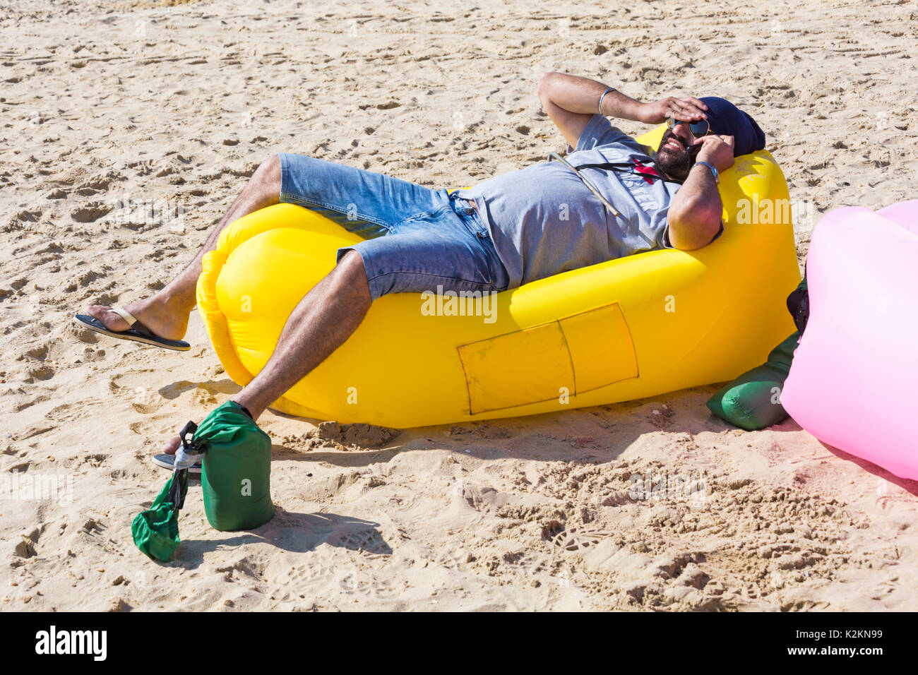 Bournemouth, Dorset, UK. 1st Sep, 2017. UK weather: lovely warm sunny day at Bournemouth beach on the South Coast. Man relaxing on yellow inflatable couch lounger talking on mobile phone. Credit: Carolyn Jenkins/Alamy Live News Stock Photo