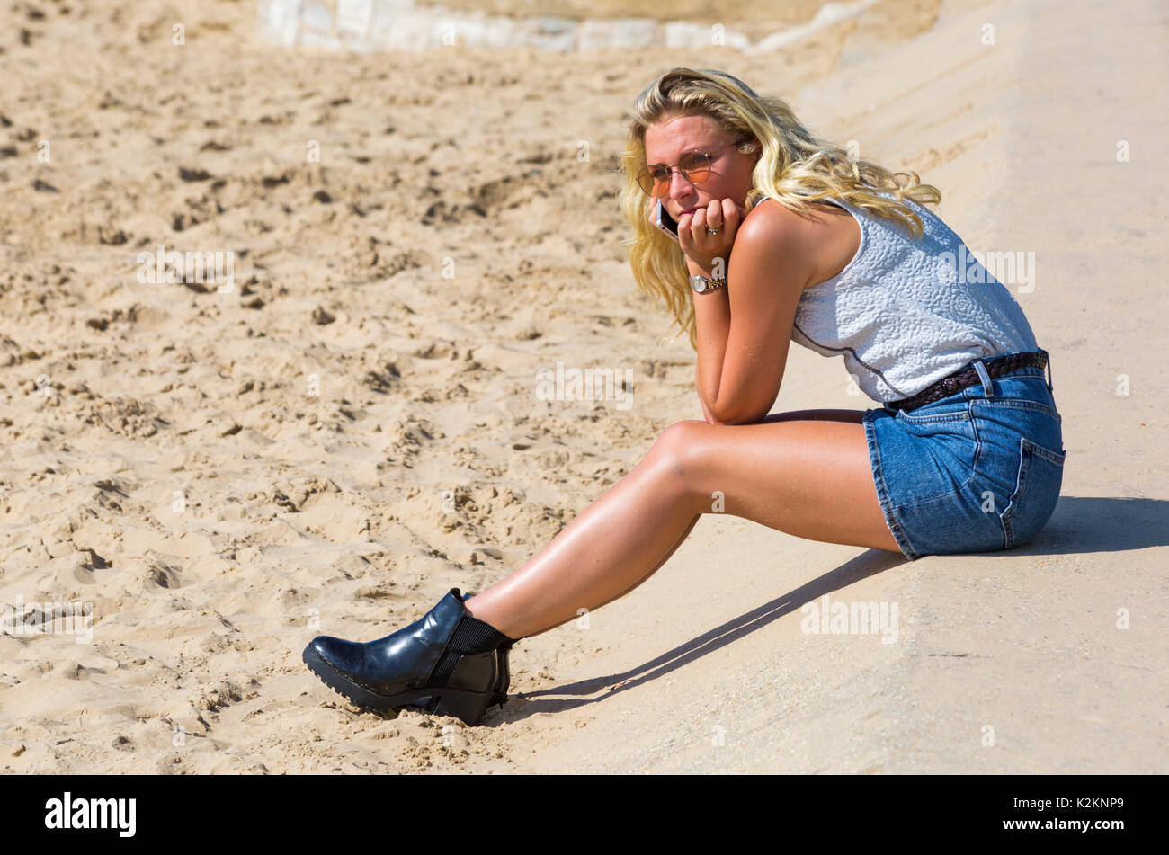 Bournemouth, Dorset, UK. 1st Sep, 2017. UK weather: lovely warm sunny day at Bournemouth beach - visitors get there early to get a good spot. Attractive young woman with long blond hair wearing mini denim skirt sitting by beach holding mobile phone to her ear.  Credit: Carolyn Jenkins/Alamy Live News Stock Photo