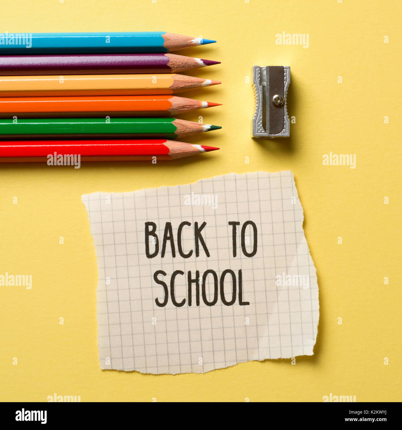 high-angle shot of some pencil crayon of different colors, a metallic sharpener and a note with the text back to school on a yellow background Stock Photo
