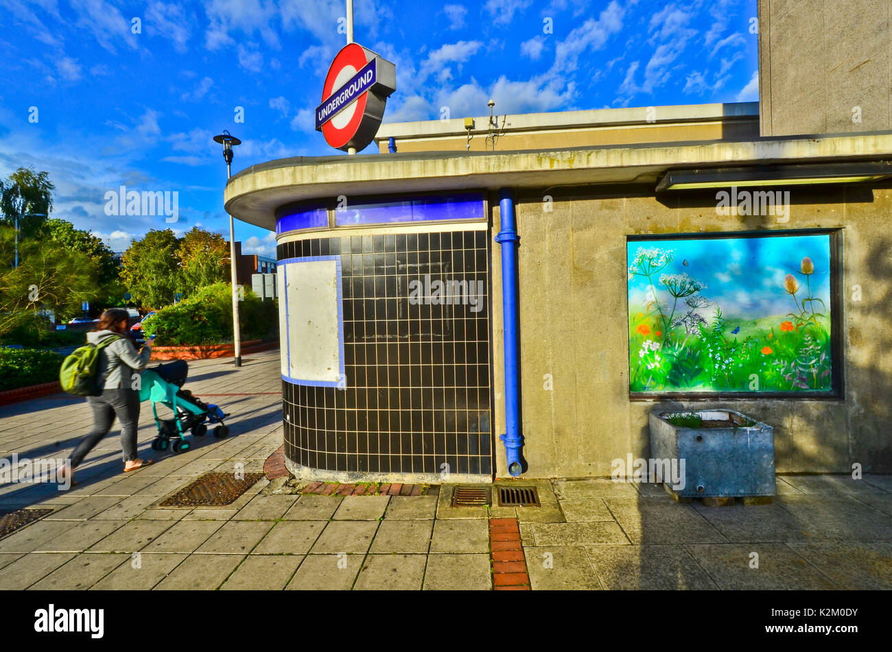 Wanstead Central line underground station with a mural of countryside on the wall. An old water tank is used as a planter. Stock Photo