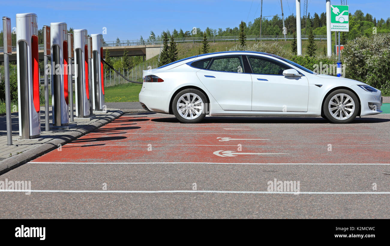 PAIMIO, FINLAND - JUNE 3, 2017: White Tesla Model S electric car charges battery on Tesla Supercharger Station in Paimio, Finland on a sunny day. Stock Photo