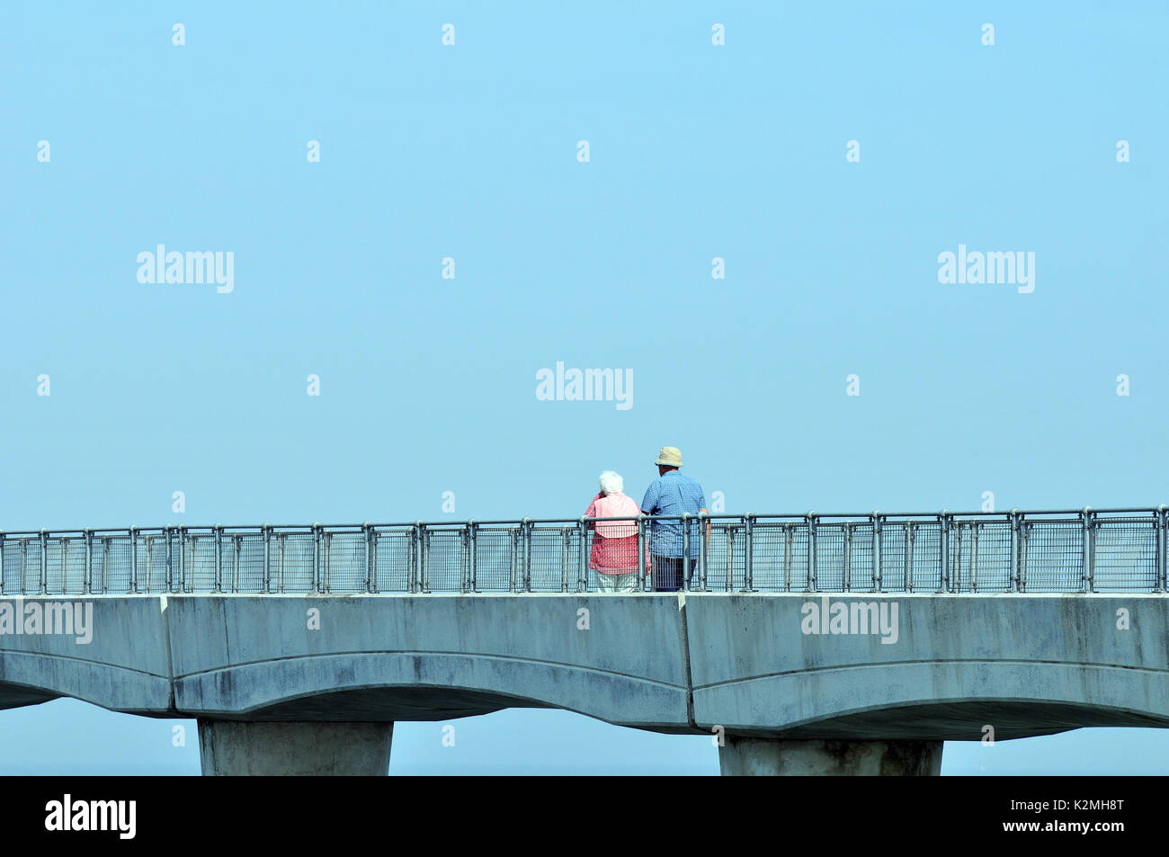 A retired elderly older couple out walking along a bridge pathway hand ...