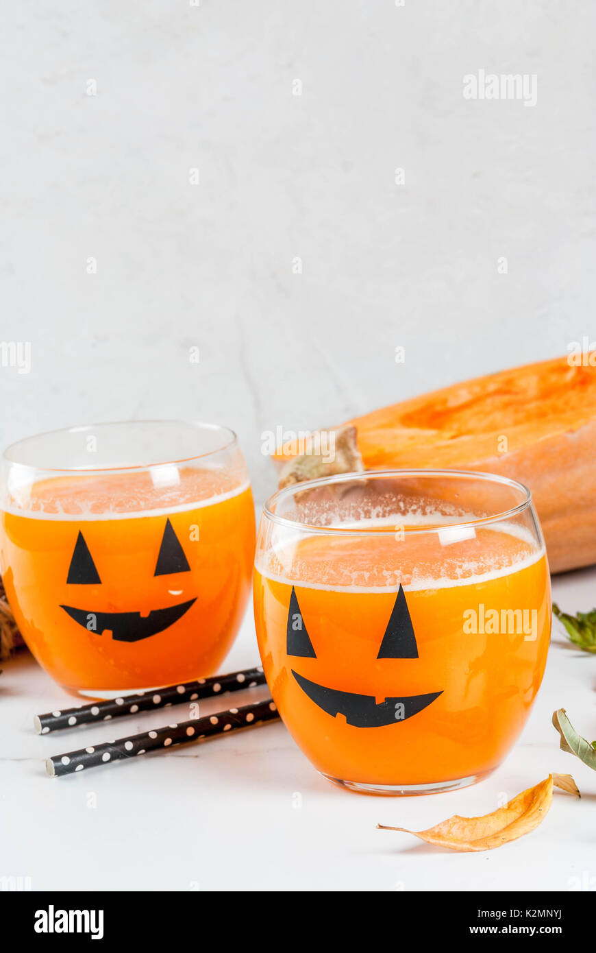 Ideas for a children's and party of Halloween treats. Pumpkin orange cocktail in glasses, decorated with a pumpkin jack lantern, on a white marble tab Stock Photo