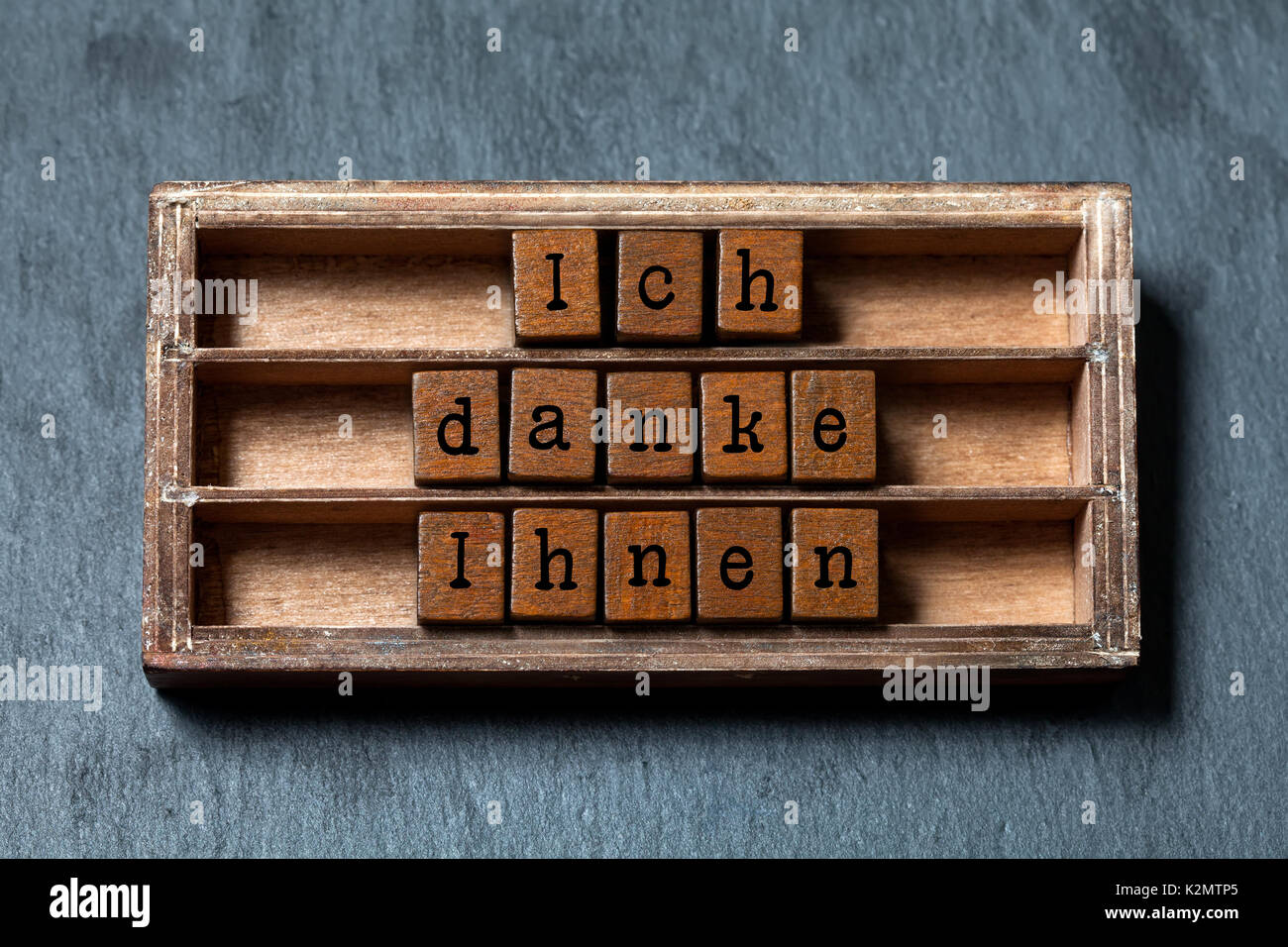 Ich danke Ihnen. Thank you in German translation. Vintage box, wooden cubes thankful phrase message written with old style letters. Gray stone textured background. Close-up, up view, soft focus Stock Photo