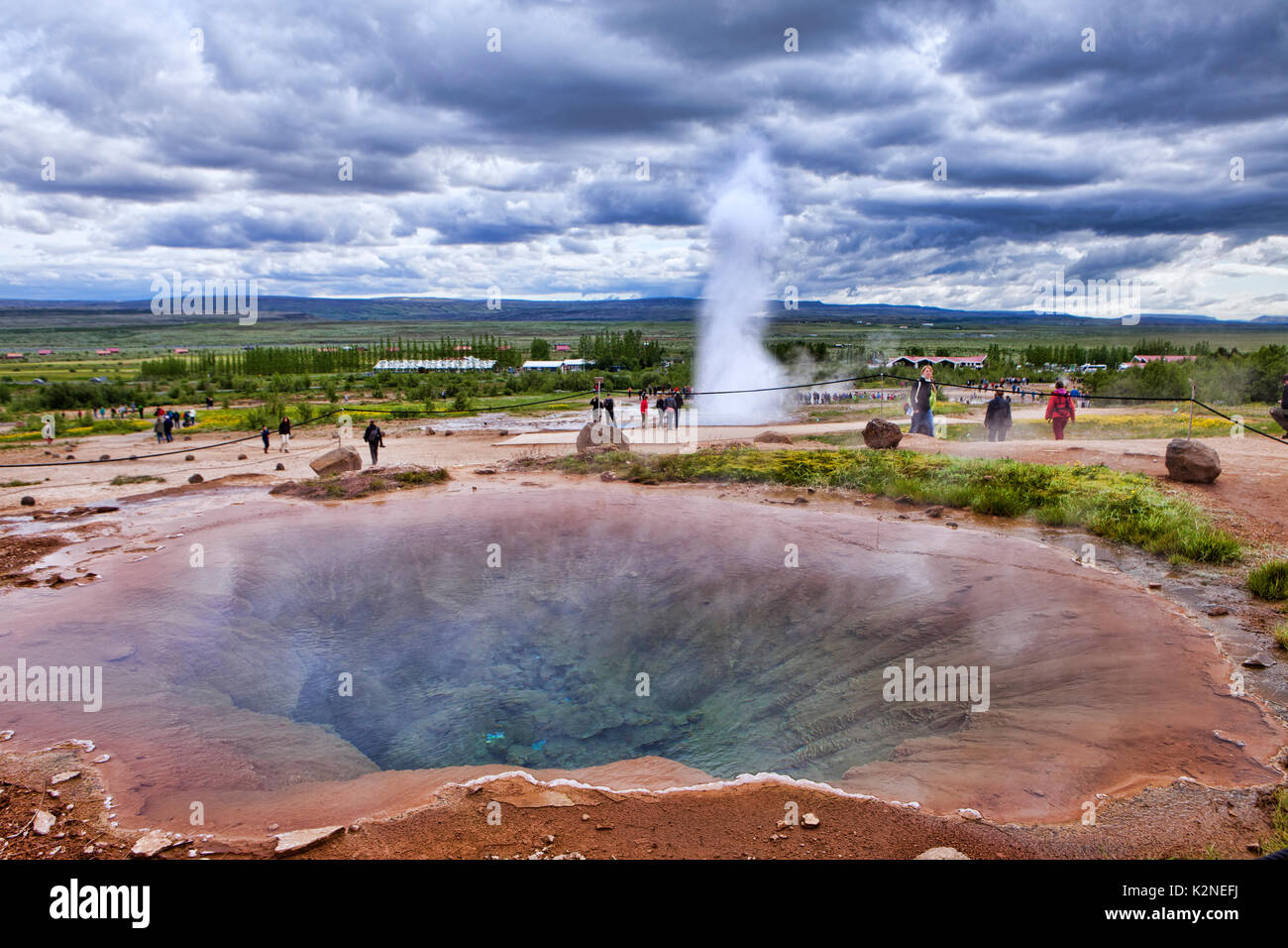 Image of a calm geyser hole with an erupting geyser behind it in Gysir, Iceland. Stock Photo