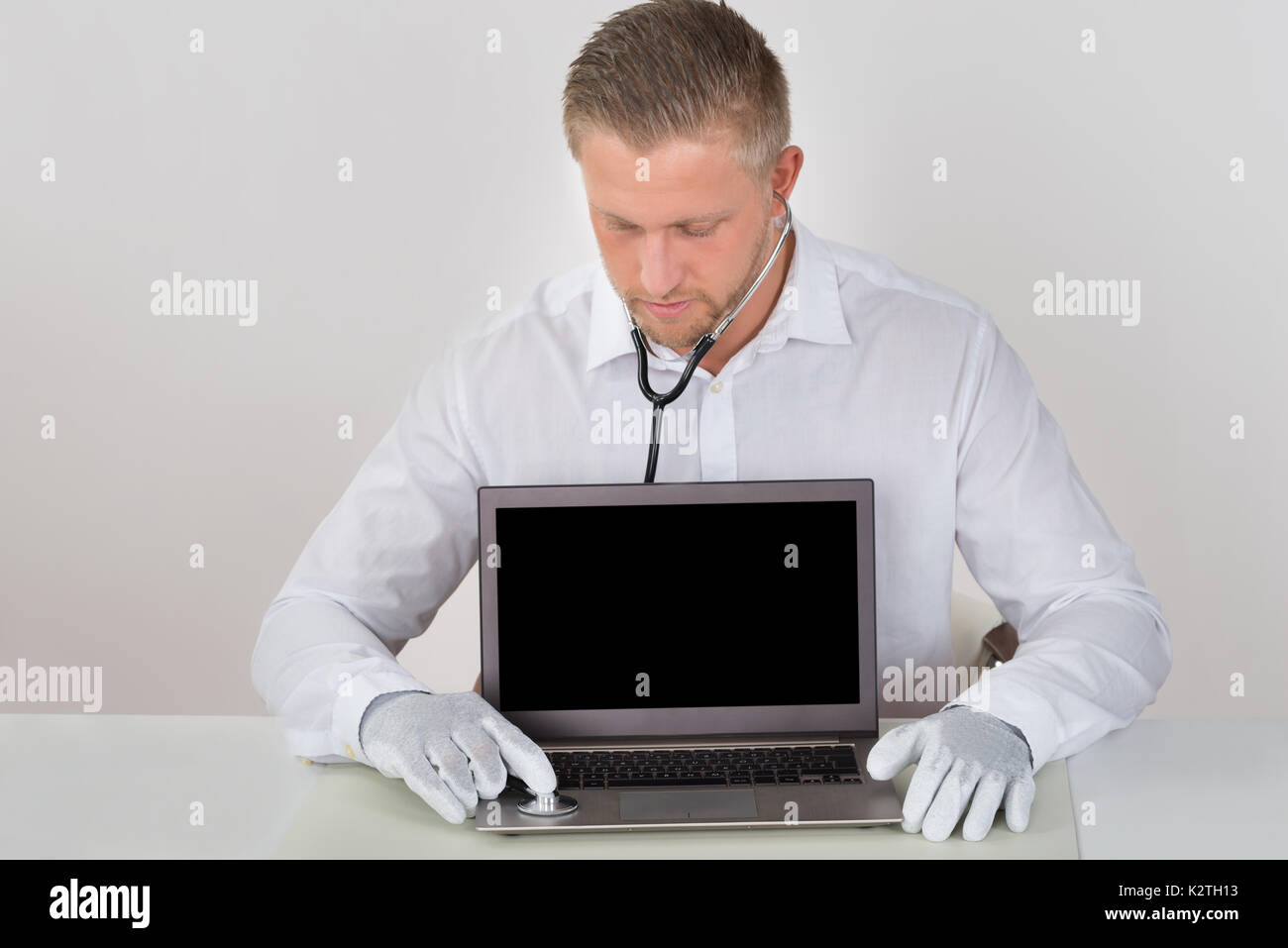 Young Male Technician Examining Laptop With Stethoscope At Desk Stock Photo
