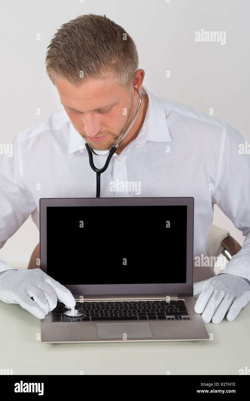 Young Male Technician Examining Laptop With Stethoscope At Desk Stock Photo
