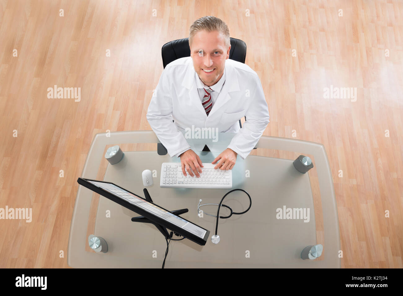 Happy Young Doctor Working On Computer At Desk Stock Photo