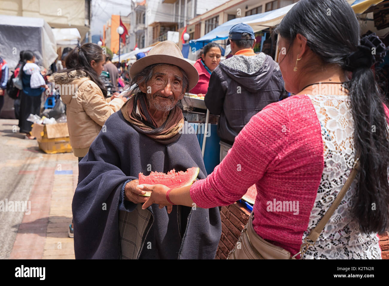 May 6, 2017 Otavalo, Ecuador: a woman hands over a slice of watermelon to a poor indigenous man Stock Photo