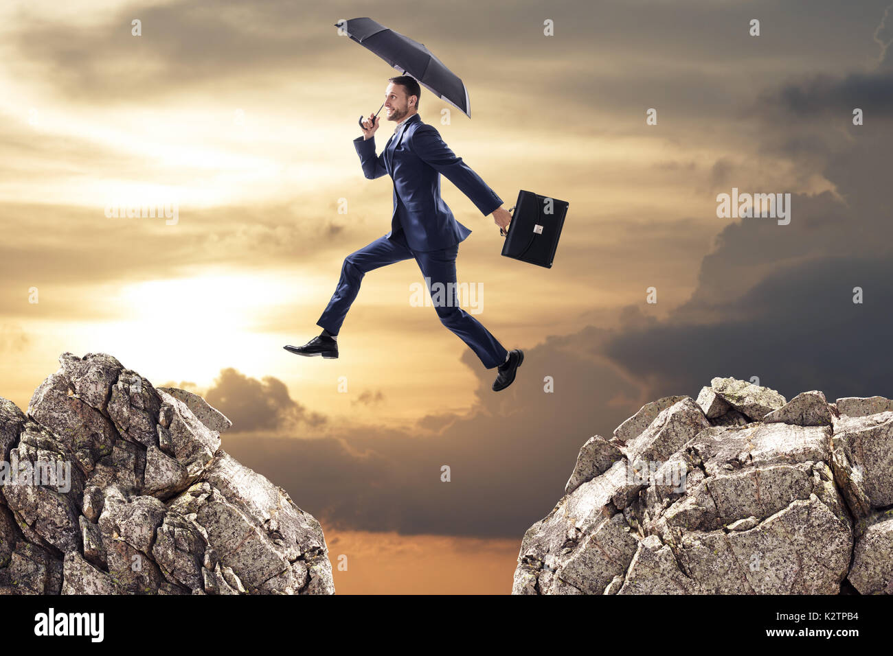 Business man jumping over a cliff with umbrella. Stock Photo