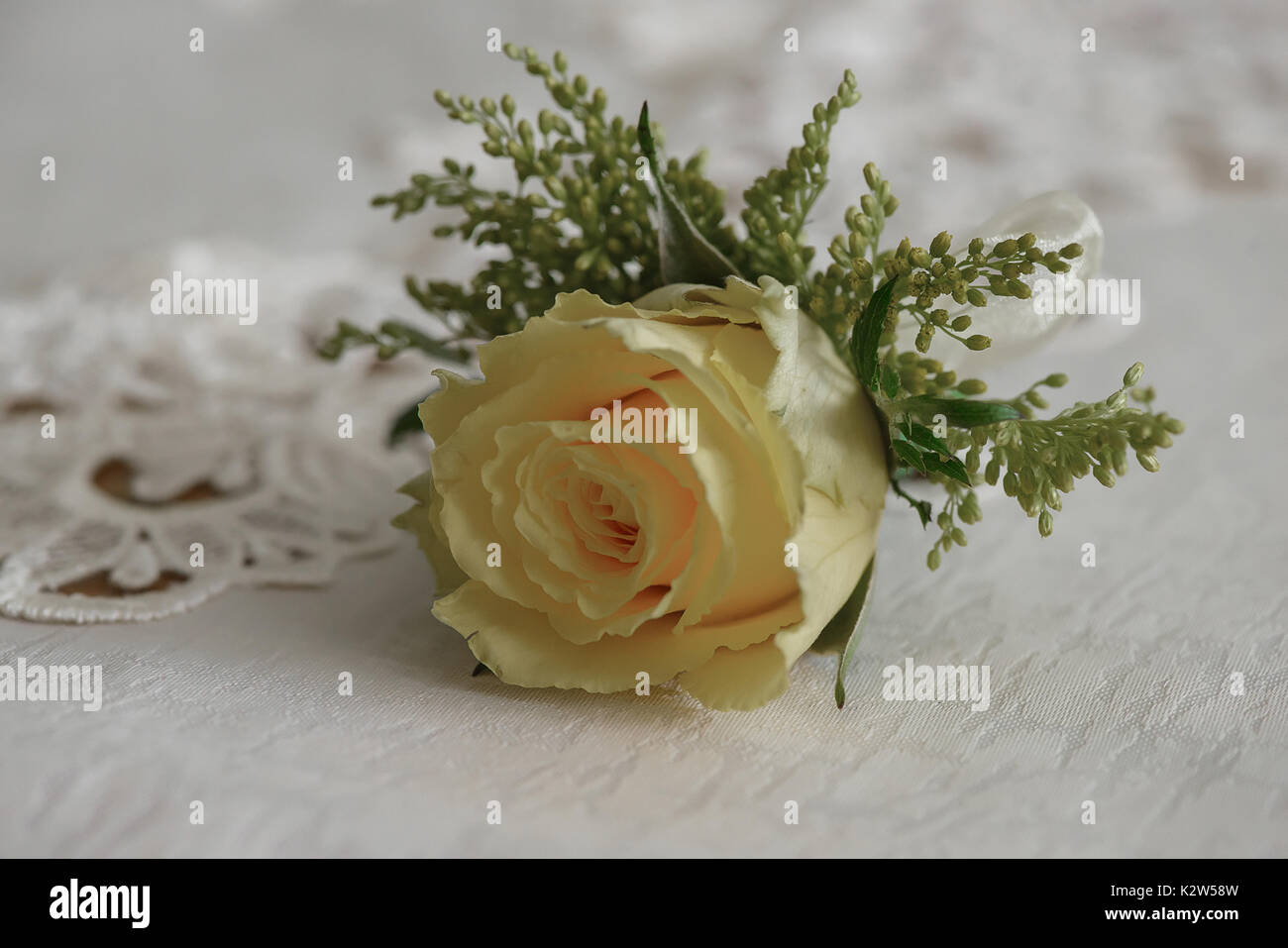 Wedding accessories: fresh yellow rose small bouquet for buttonhole used for groom and wedding guests positioned on a white cloth, in natural light Stock Photo