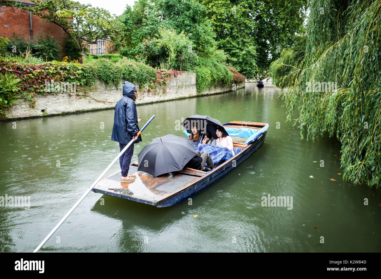 Punting in the Rain. Wet Weather Punting, Tourists take guided punts on the River Cam in rain, in Cambridge UK Stock Photo