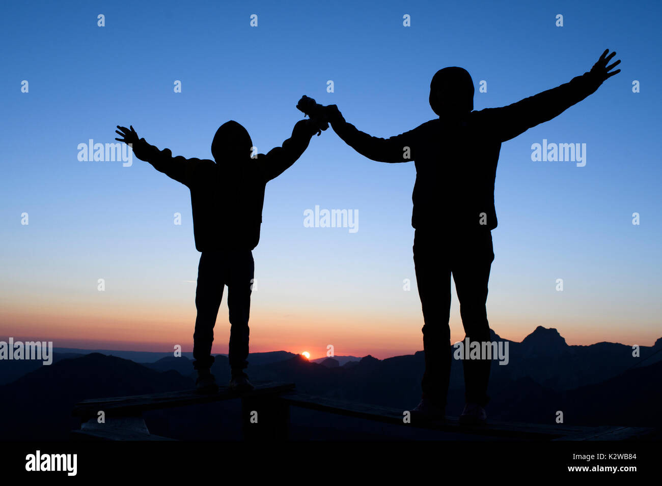 A silhouette of two people infornt of a setting sun Stock Photo