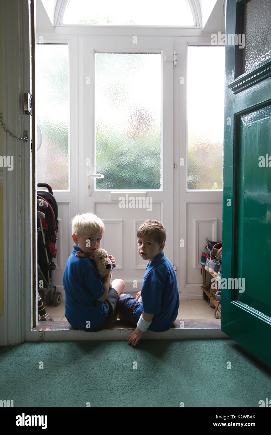 3 year old and 6 year old boys sitting in a residential doorway dressed in uniform ready to go back to school, London, England, UK Stock Photo