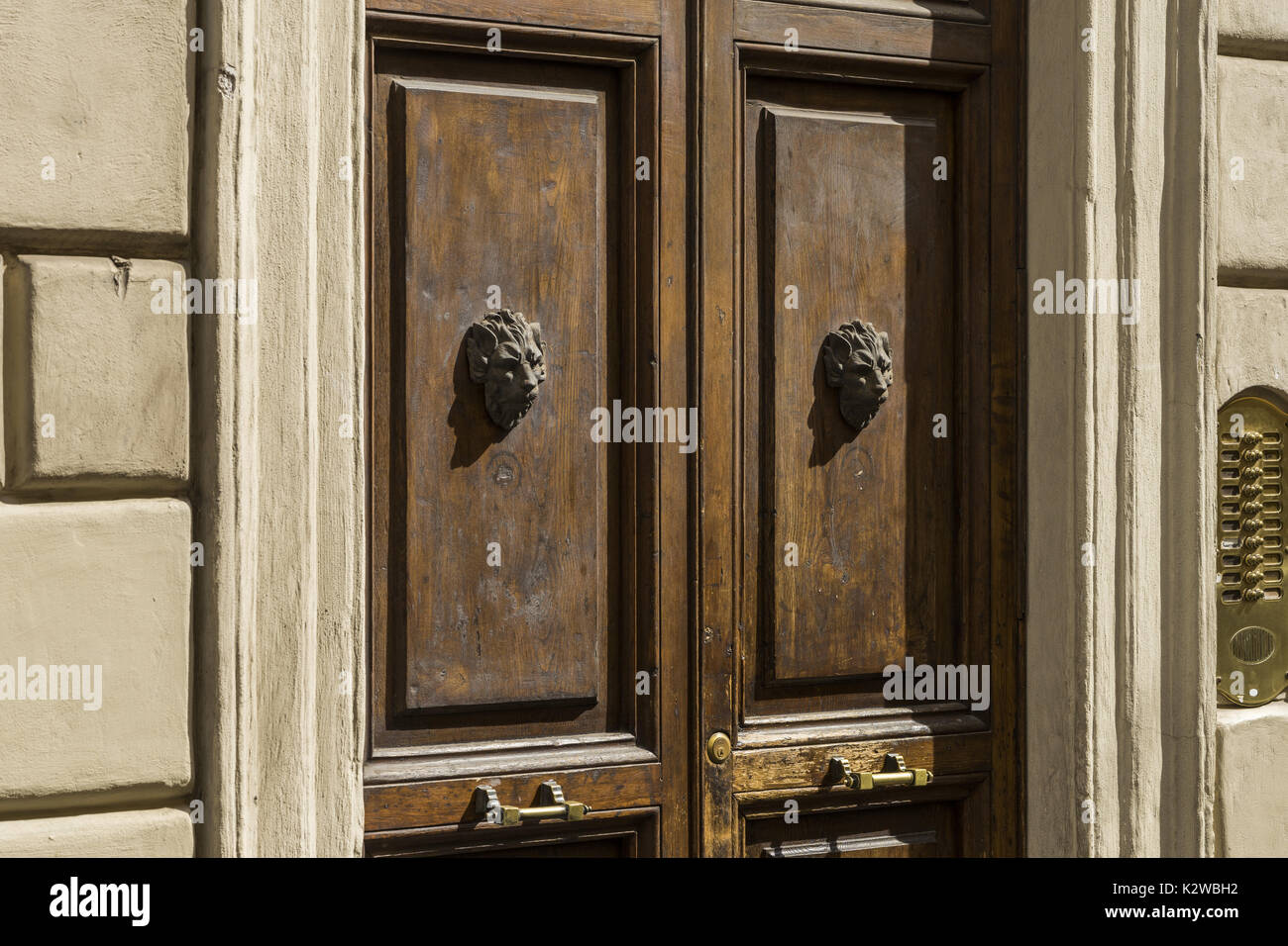 Old wooden front door decorated with two lion heads of metal. Part of the facade of the old building. Rome, Italy Stock Photo