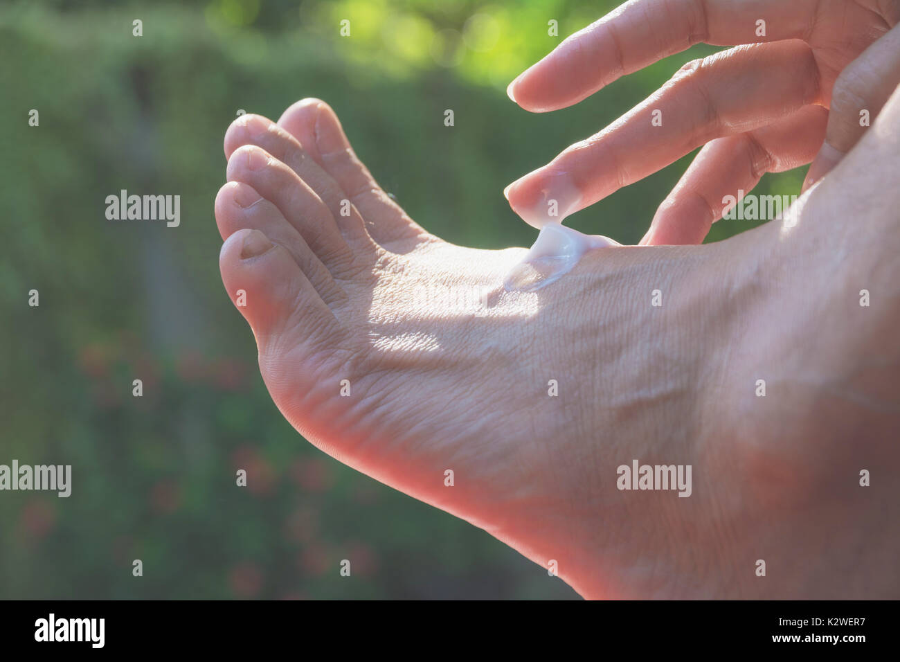 hand of woman apply lotion on skin of back foot on nature background