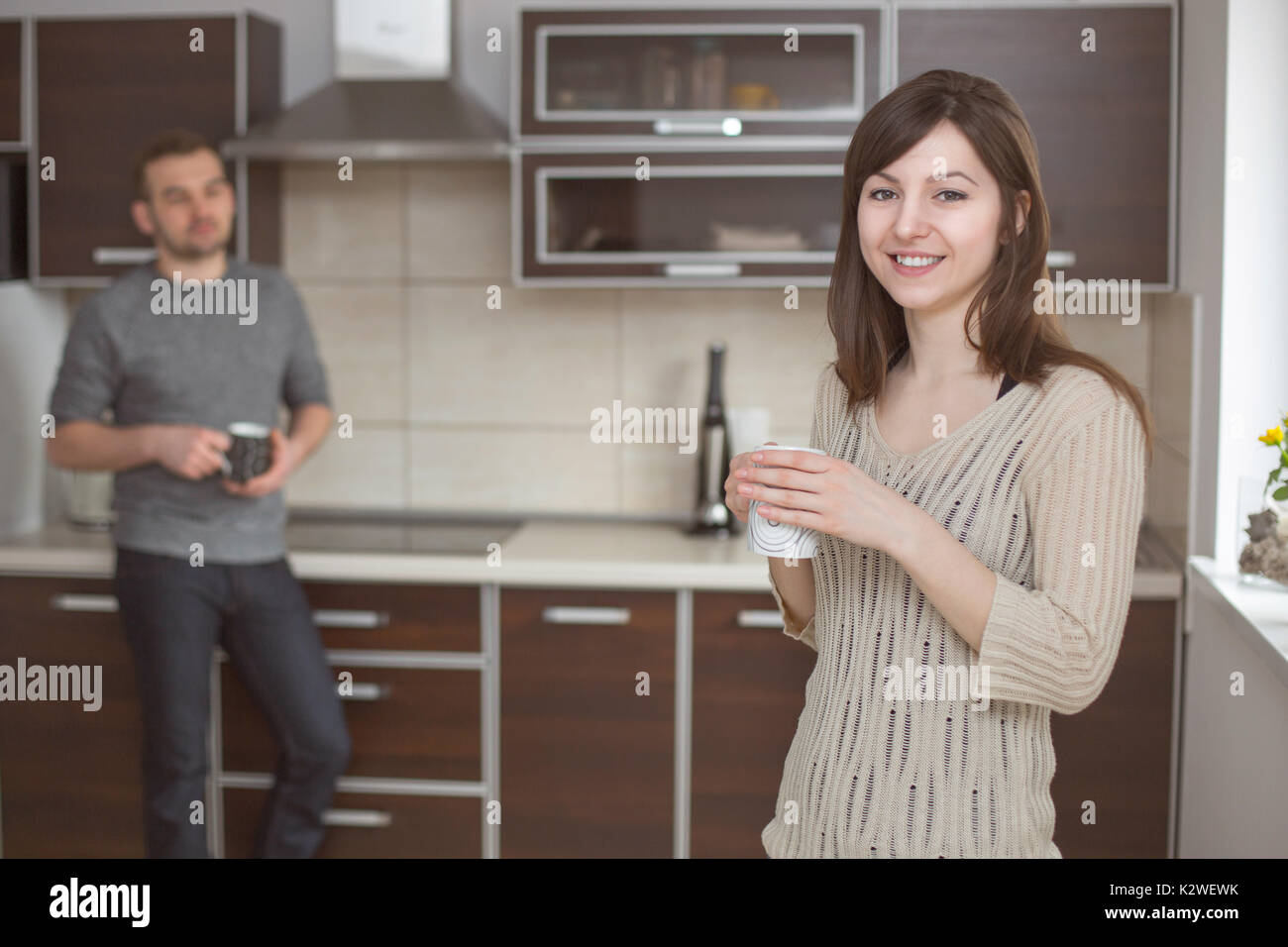 Smiling woman in kitchen with blurred man Stock Photo