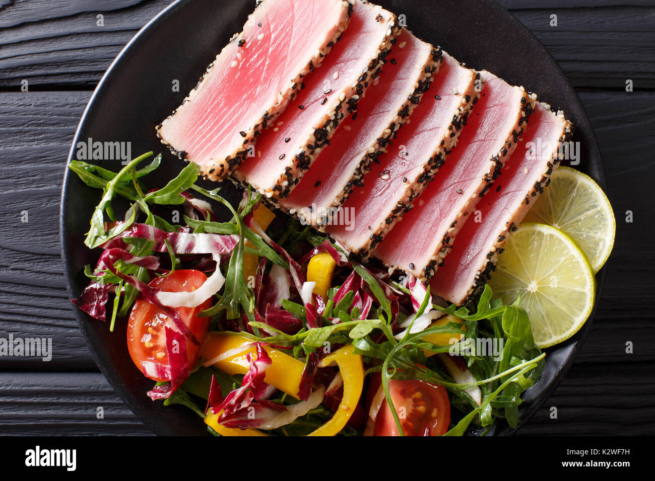 Seared ahi tuna coated sesame seeds with salad on black plate closeup. Top view from above