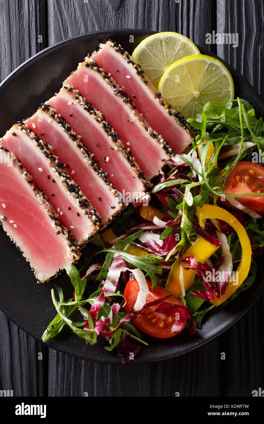 Seared ahi tuna coated sesame seeds with salad on black plate closeup. Top view from above