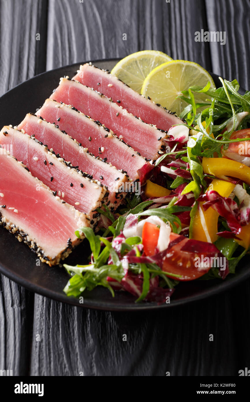 Seared ahi tuna coated sesame seeds with salad on black plate closeup. vertical Stock Photo Alamy