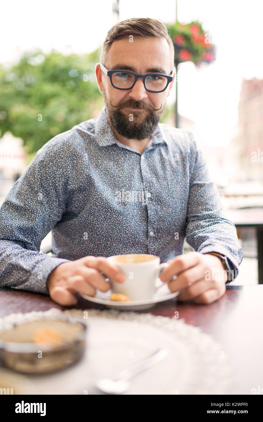 Bearded man sitting in cafe-garden and having cappuccino Stock Photo