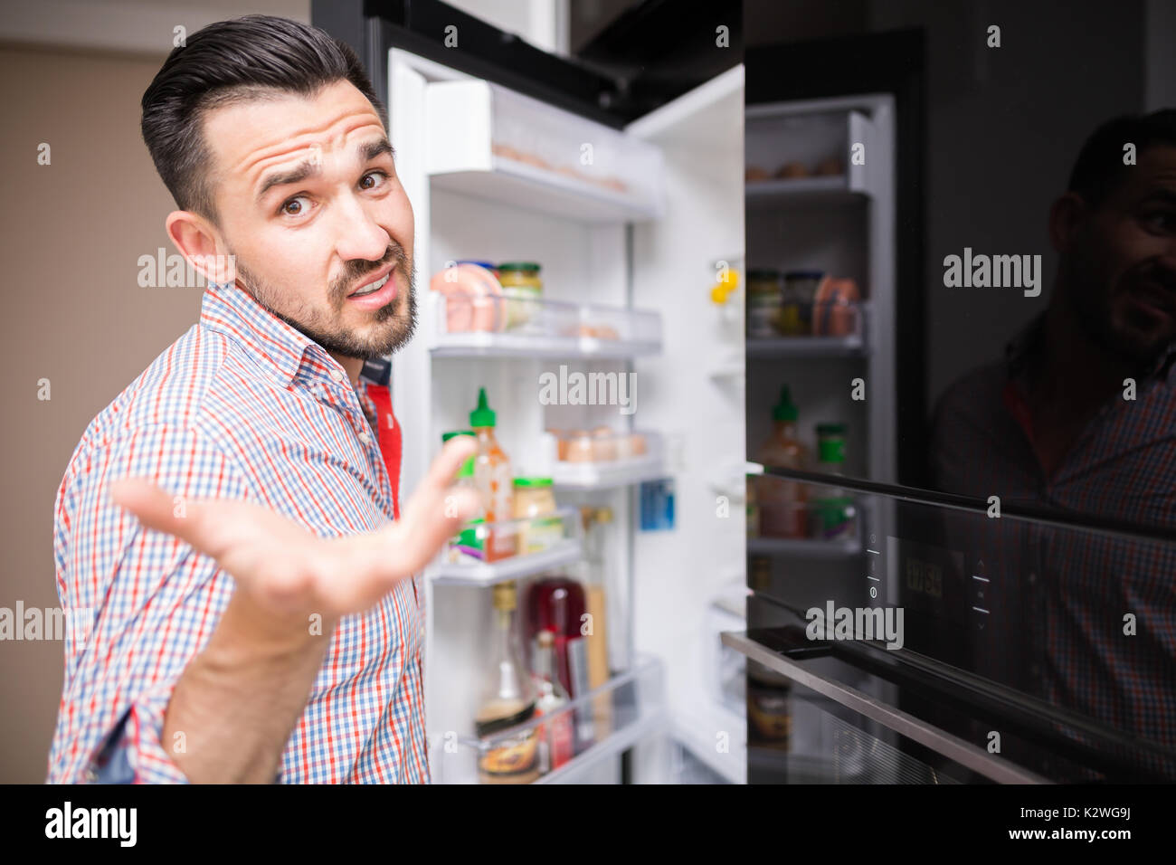 Confused young man opening fridge. Stock Photo