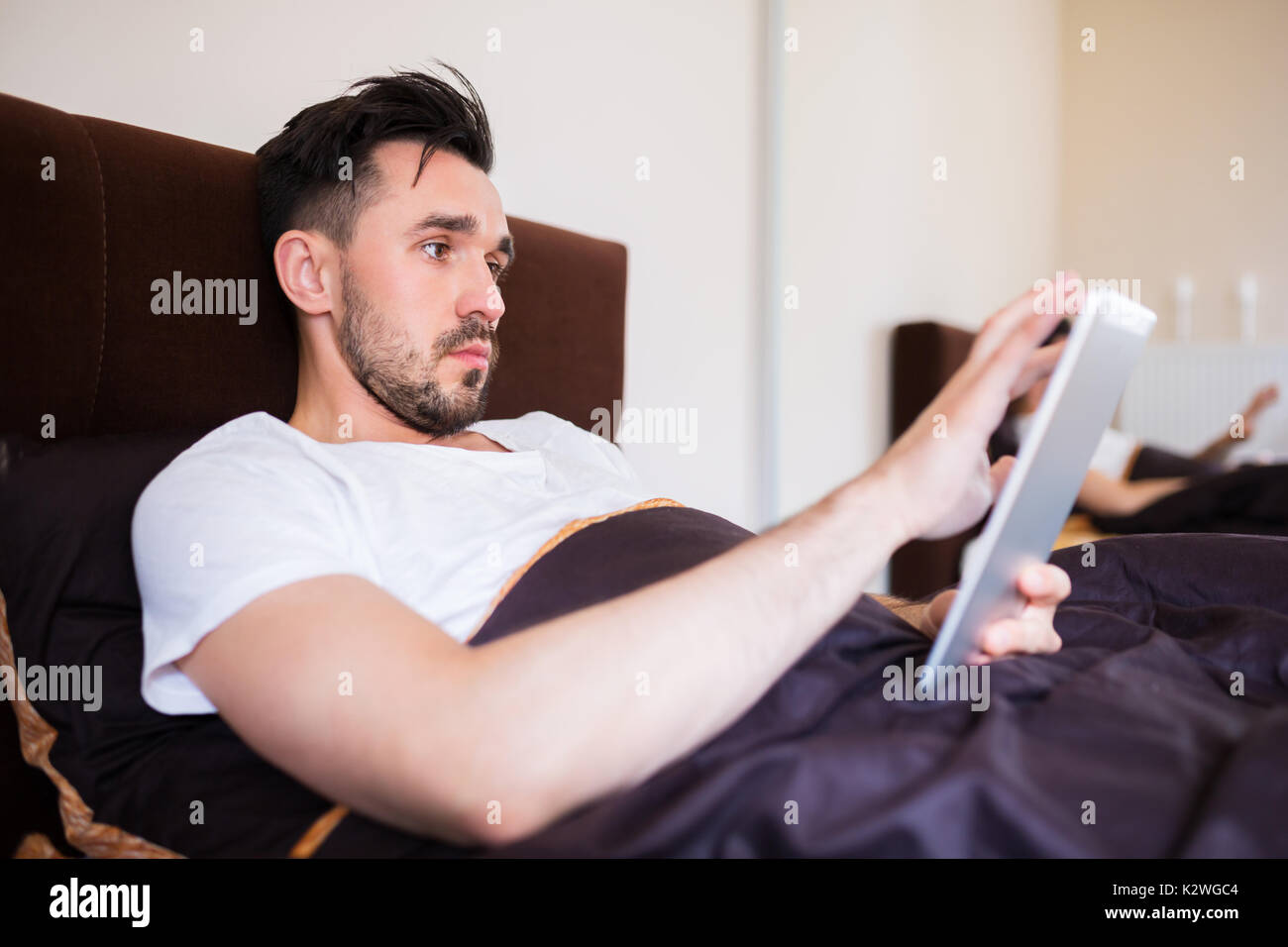 Man surfing the net on tablet in bed Stock Photo