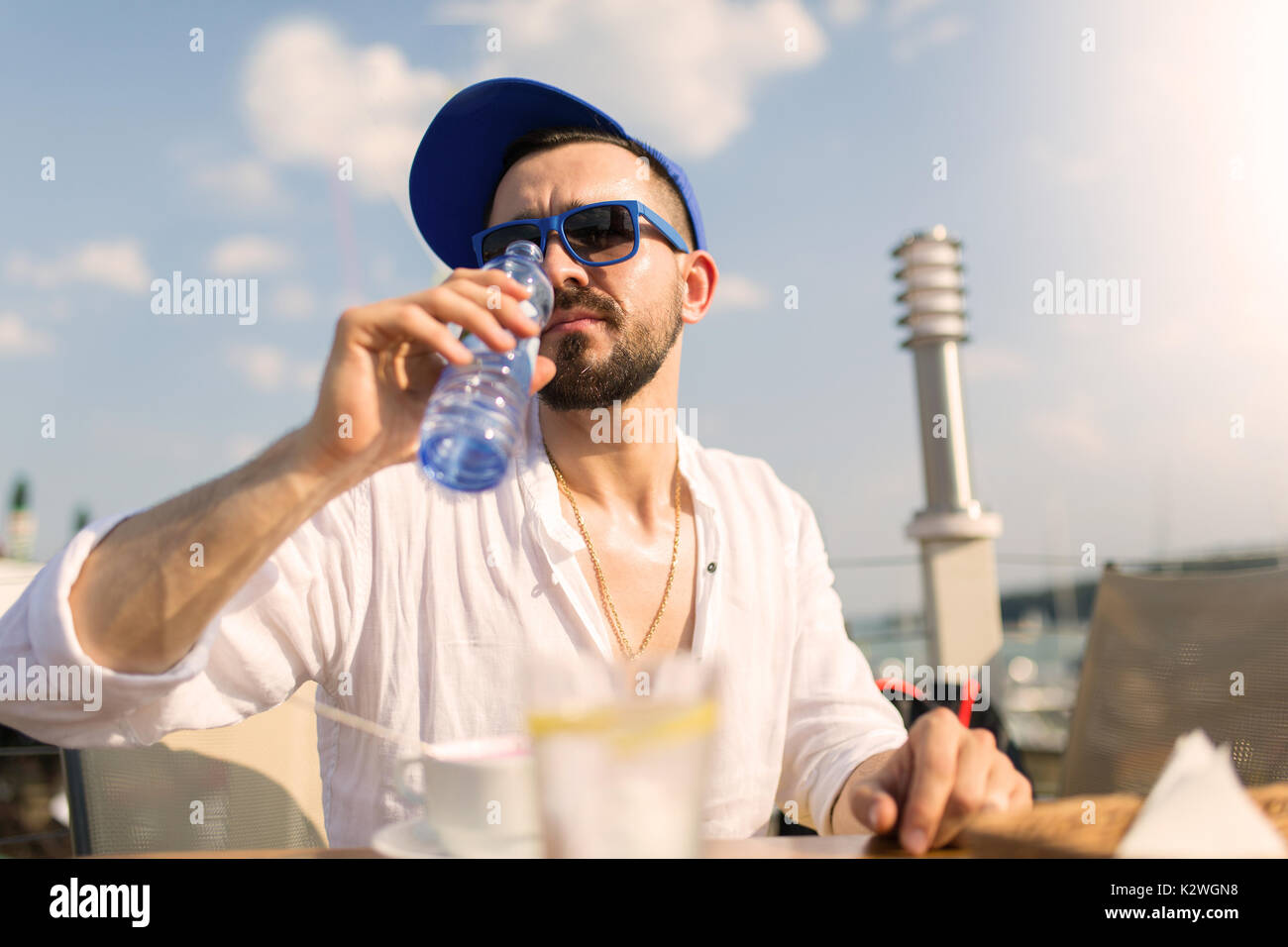 Young man drinking mineral water in outdoor restaurant during extremely hot day Stock Photo