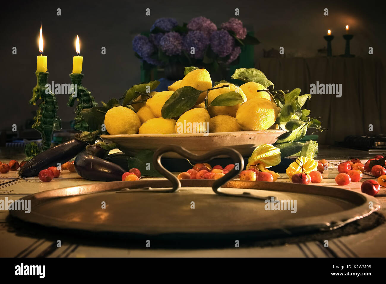 BEAUTIFUL STILL LIFE WITH CANDLES, LEMONS, CHERRIES FLOWERS IN A LOVELY SETTING OF AN ANTIQUE KITCHEN IN ITALY. Stock Photo