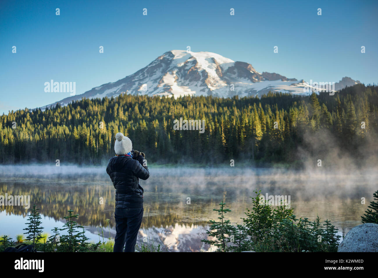 The woman photographer is taking pictures of the mountain and lake at Reflection Lakes and Mount Rainier National Park, Washington. Stock Photo