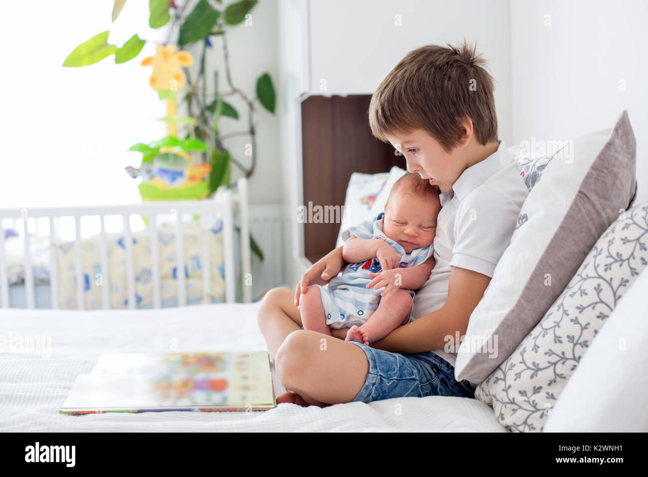 Sweet preschool boy, reading a book to his newborn brother, sitting on