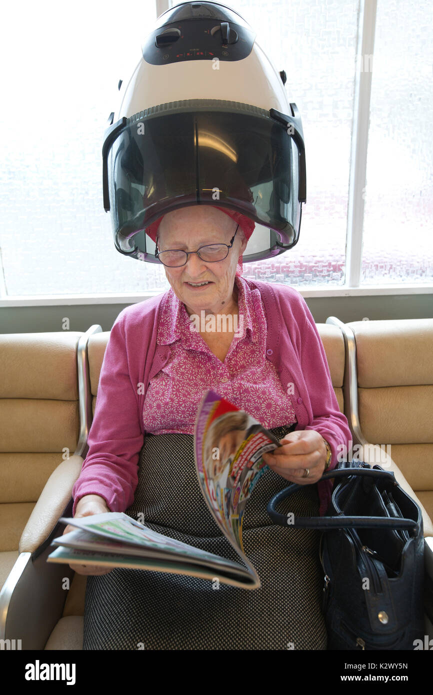 Elderly pensioner having her hair dried in a hood dryer wearing curlers at a ladies hairdresser's salon, England, United Kingdom Stock Photo