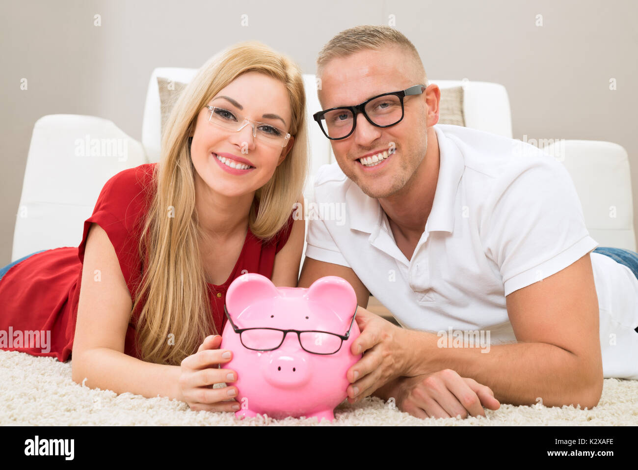 Portrait Of Happy Couple With Piggybank Lying On Carpet Stock Photo - Alamy