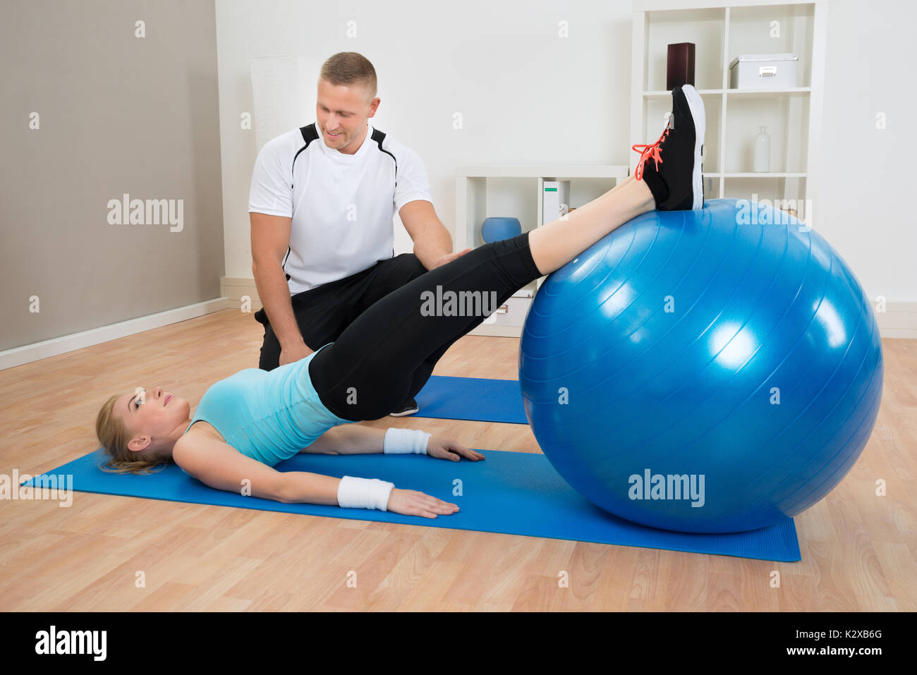 Male Instructor Looking At Woman Exerting With Pilate Ball Stock Photo
