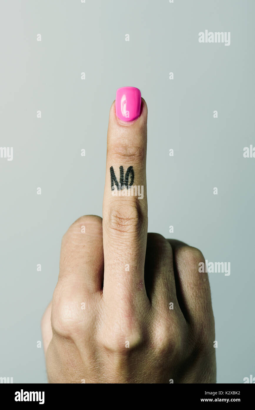 closeup of the hand of a young caucasian woman giving the middle finger with the word no handwritten in it, against an off-white background Stock Photo