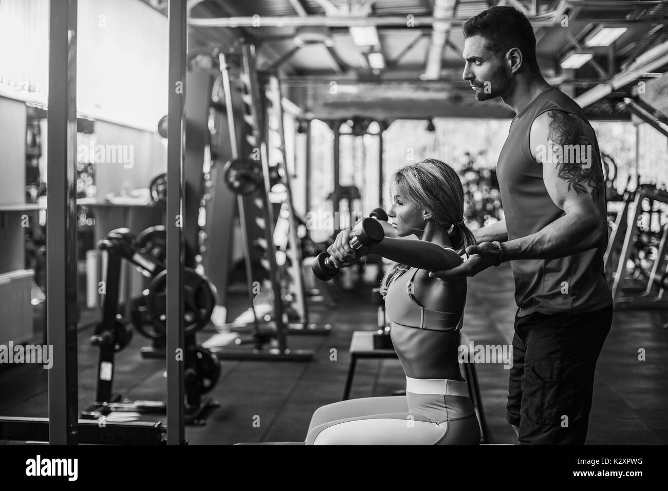 Sporty girl doing weight exercises with assistance of her personal