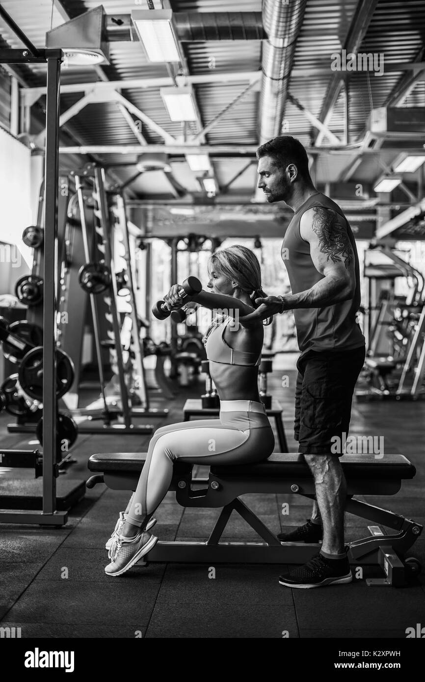 Sporty girl doing weight exercises with assistance of her personal